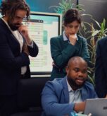 Diverse corporate employees analyzing project updates to ensure goal accomplishment, reviewing infographics on laptop and finding ways to obtain new funds. Business management team. Camera B.