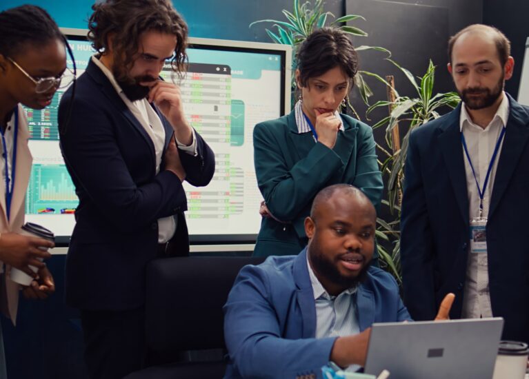 Diverse corporate employees analyzing project updates to ensure goal accomplishment, reviewing infographics on laptop and finding ways to obtain new funds. Business management team. Camera B.